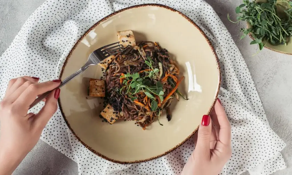 Assembled teriyaki bowl with noodles, shredded carrots, greens, and cubed protein