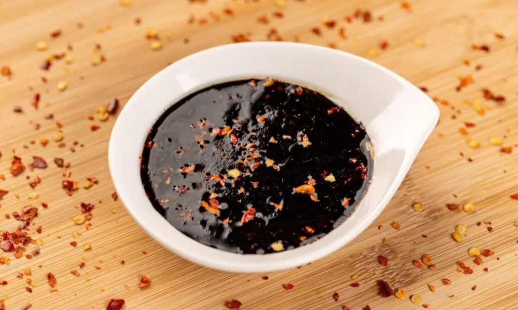 Small white dish of glossy teriyaki sauce sprinkled with red pepper flakes