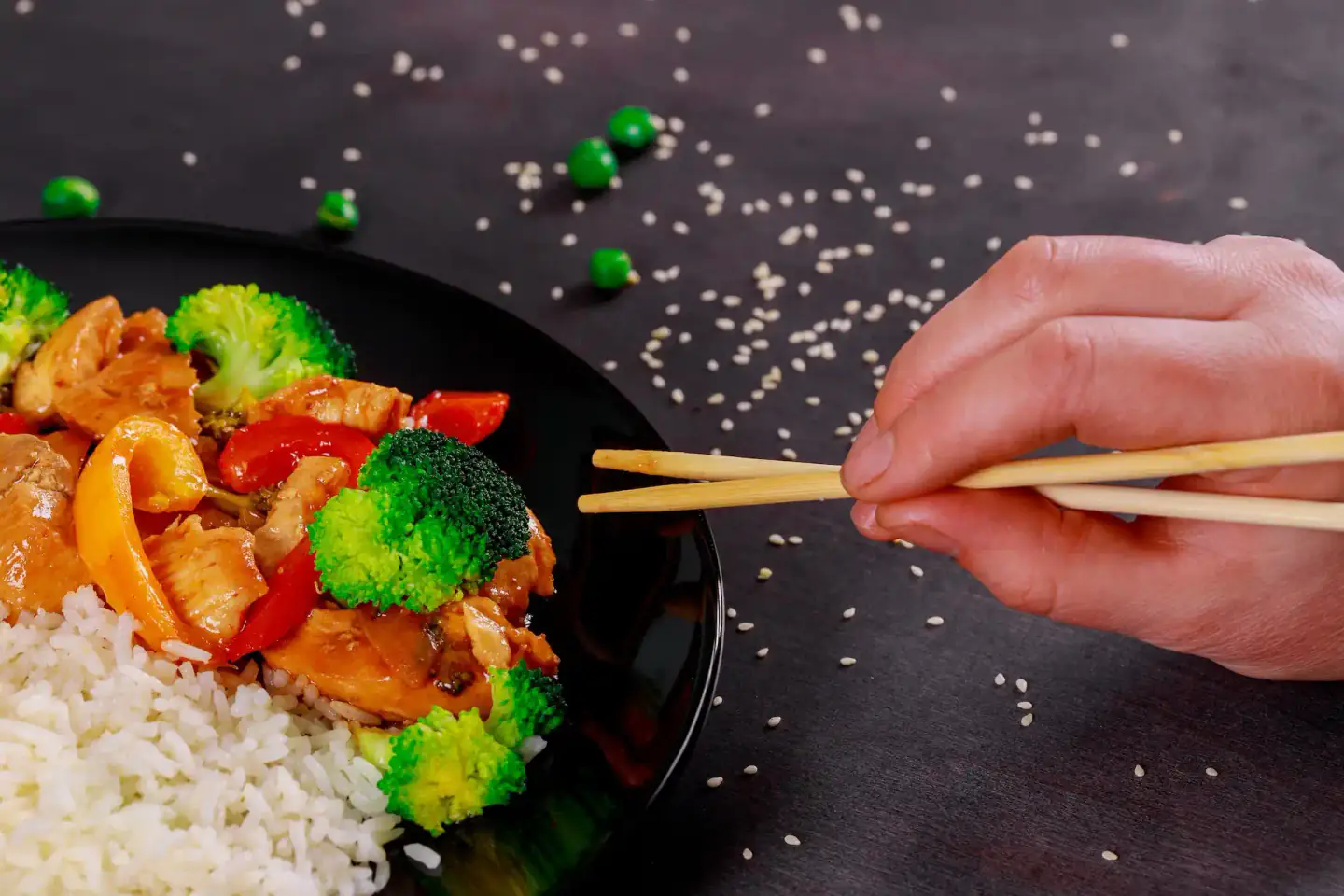 Plate of chicken and broccoli stir-fry with rice, hand holding chopsticks