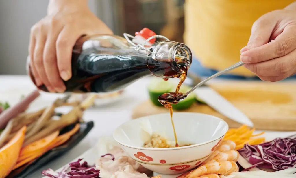 Hand pouring teriyaki sauce from glass bottle into spoon over bowl
