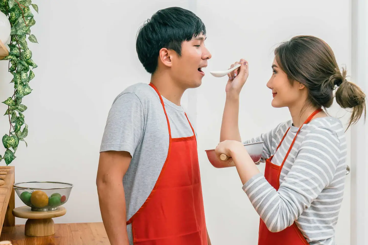 Couple in red aprons tasting food for a lunchbox