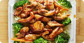 Teriyaki chicken and shrimp over rice with broccoli and carrots in takeout box