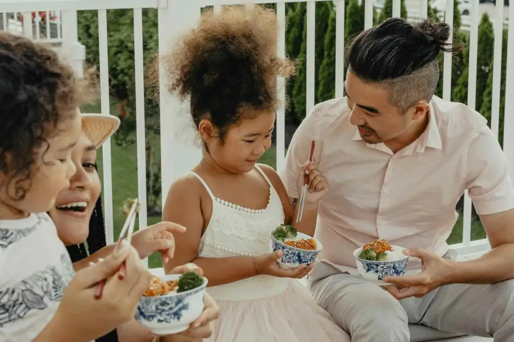 Man and children eating from blue patterned bowls on a balcony
