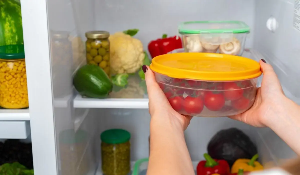 Hands placing airtight container of cherry tomatoes in refrigerator