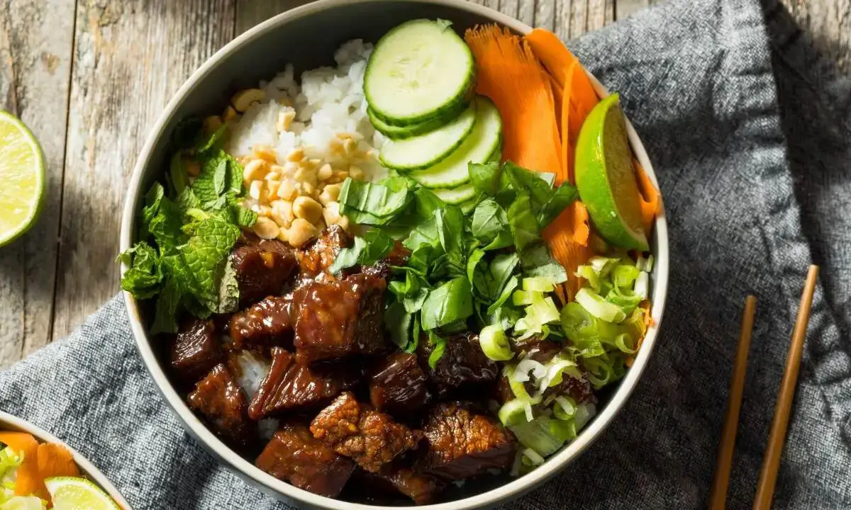 Beef teriyaki rice bowl with glazed beef, cucumber, carrots, herbs