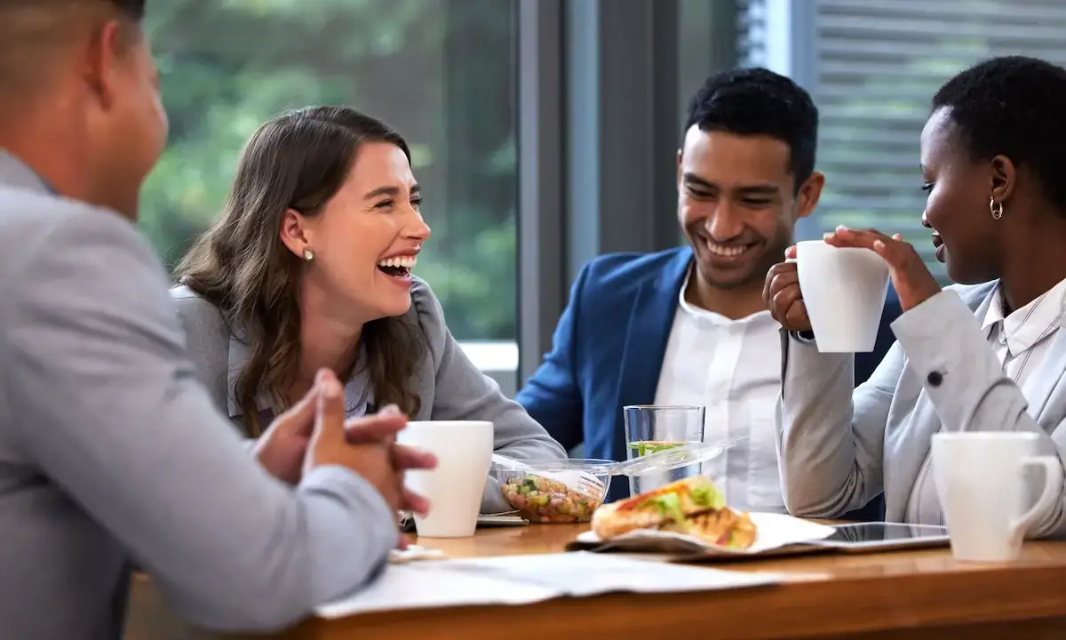 Coworkers laughing over an office lunch while planning a group catering order
