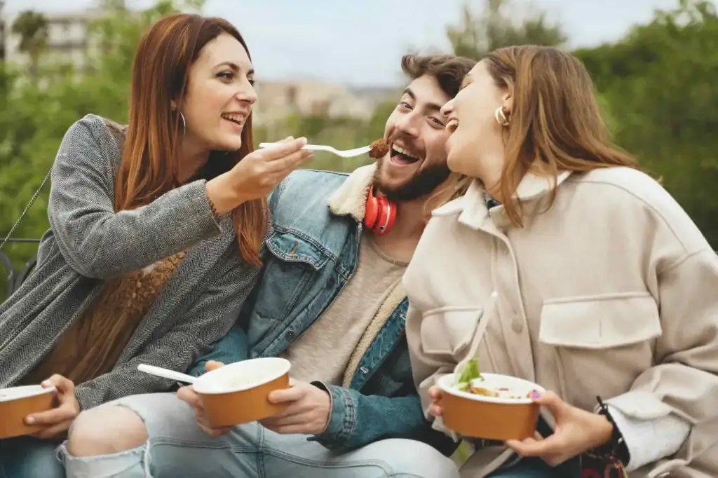 Three friends sharing takeout lunch bowls outdoors