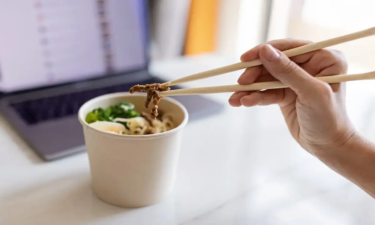 Chopsticks lifting lean teriyaki meat from a takeout bowl with noodles