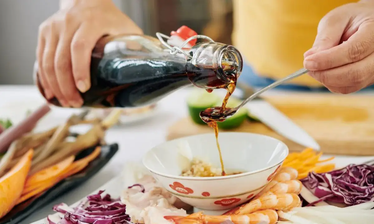 Pouring teriyaki sauce into a spoon over a bowl with shrimp and vegetables